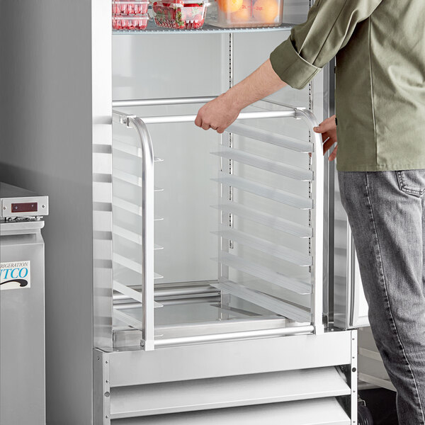 A person opening a refrigerator to reveal an aluminum sheet pan rack.