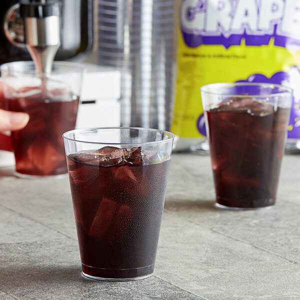 A hand pouring DominAde grape drink mix into a glass of ice.