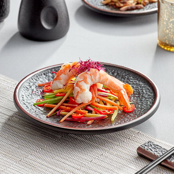 An Acopa black matte stoneware plate with shrimp and vegetables on a table.