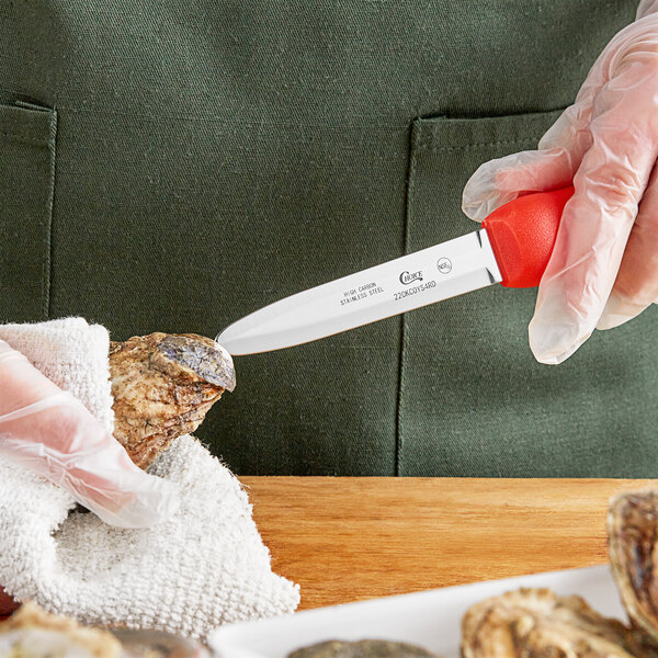 A person using a red and white Choice Galveston Oyster Knife to cut into an oyster shell.