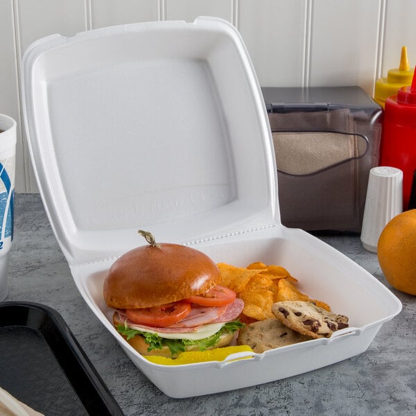 A Dart white foam hinged lid container with a sandwich and chips.