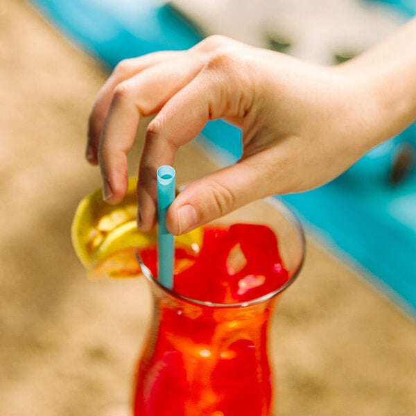A hand holding a Phade blue compostable straw in a glass with a red drink.