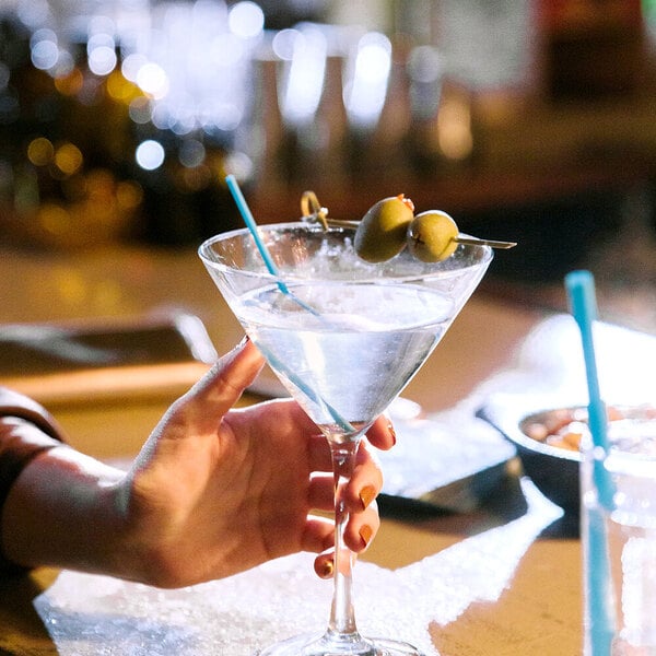A hand using a Phade blue compostable sip straw in a martini with olives.