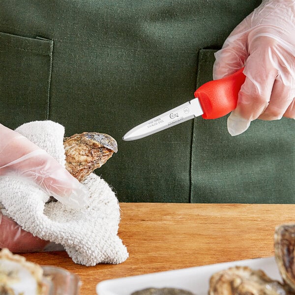A person in a plastic glove using a Choice Boston Style Oyster Knife to cut up an oyster.