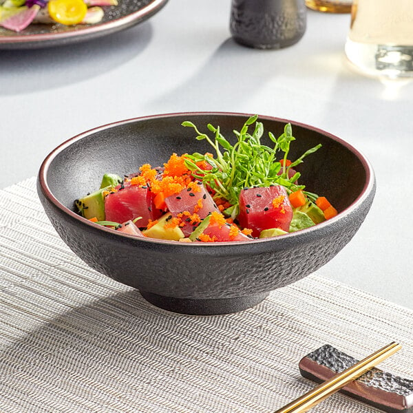 An Acopa black stoneware bowl filled with sushi on a table.