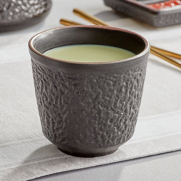 A black Acopa stoneware mug filled with green tea on a table.