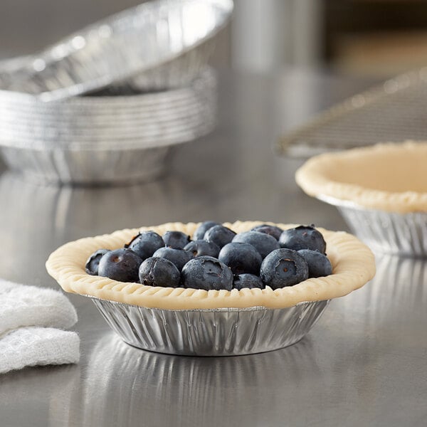 A blueberry tart in a Baker's Mark foil tin on a table.