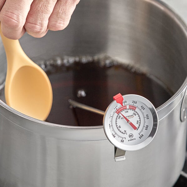 A hand using an AvaTemp candy thermometer to check liquid temperature.