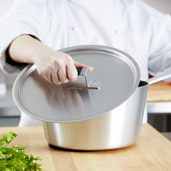 A chef using a Vollrath Wear-Ever aluminum pot lid over a pot.