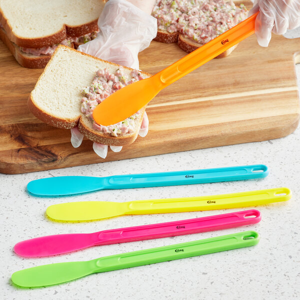 A person spreading food on a sandwich with a Choice sandwich spreader with neon handles.