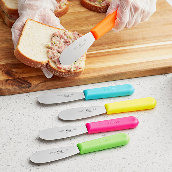 A yellow, blue, and green Choice sandwich spreader being used to spread on a sandwich.