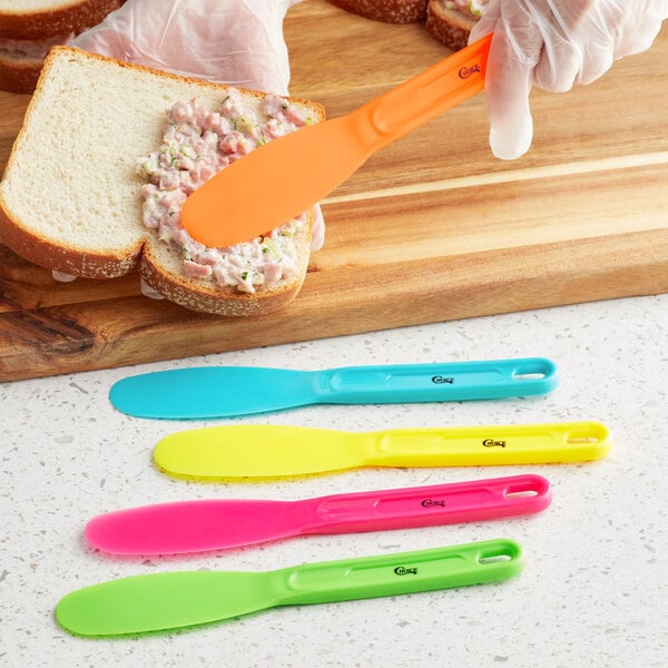 A hand using a Choice neon yellow sandwich spreader to spread on a sandwich.
