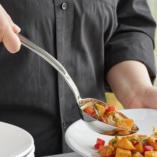 A person using a Vollrath stainless steel oval serving spoon to serve food onto a white plate.