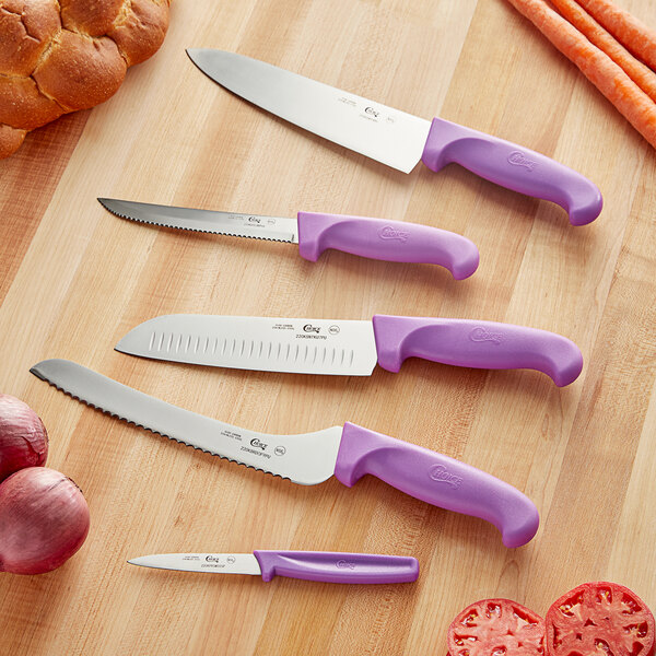 A Choice knife set with purple handles on a table with carrots and onions.