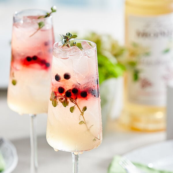 A glass of Monin elderflower syrup with a drink and berries on the side.
