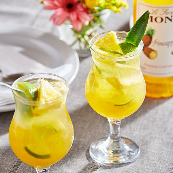 Two glasses of yellow tropical drinks with pineapple and limes.