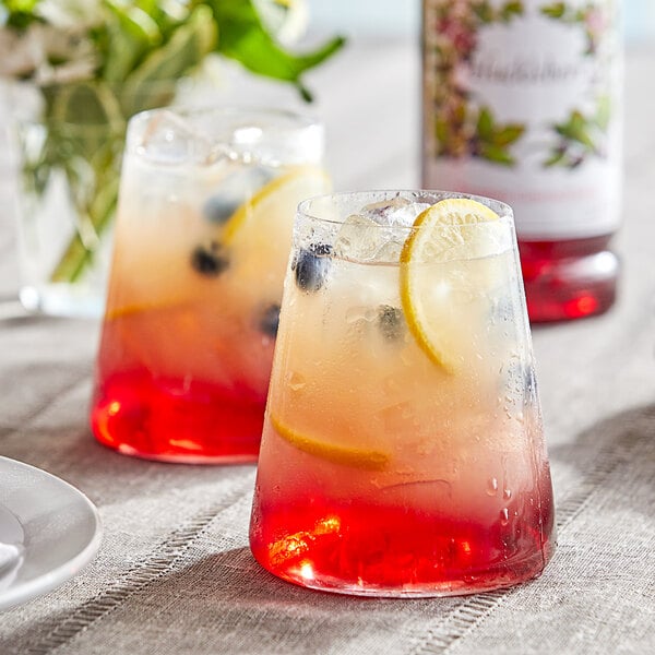Two glasses of Monin huckleberry syrup with fruit and ice.