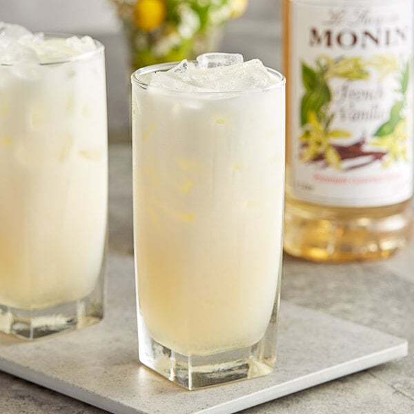 A glass of milk with Monin French Vanilla syrup next to a bottle of Monin French Vanilla syrup.