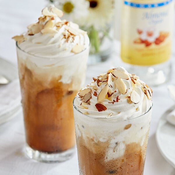 Two glasses of brown drinks with whipped cream on top.