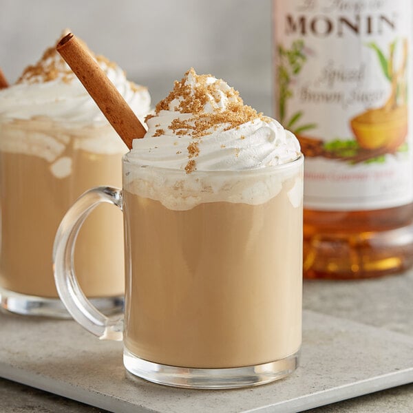 A glass mug of coffee with Monin Spiced Brown Sugar syrup and whipped cream with a cinnamon stick.
