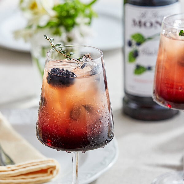 A glass of red liquid with ice and a black berry on top.