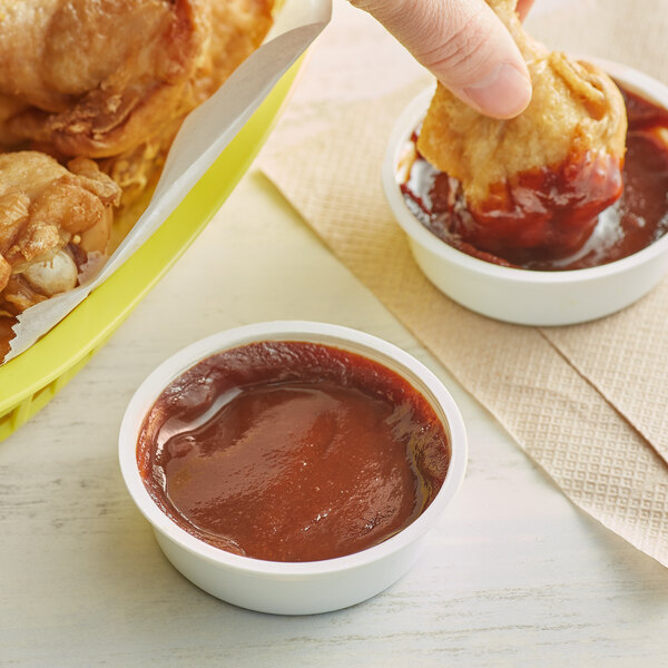 A person dipping a piece of fried chicken into a bowl of Cattlemen's Kansas City Classic BBQ sauce.