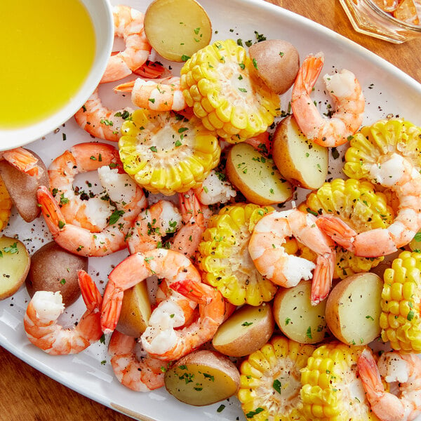 A bowl of liquid with shrimp, corn on the cob, and lemon.