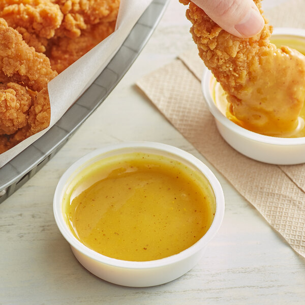 A person dipping a French's honey mustard sauce into a bowl of fried chicken.