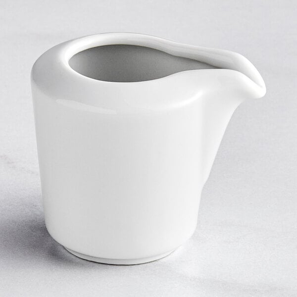 A Bauscher bright white porcelain creamer with a handle and spout on a white surface.