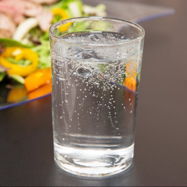 A Libbey seltzer glass filled with bubbly water on a table with a salad.