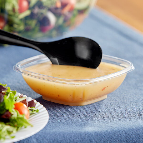 A clear Visions plastic bowl of salad with a spoon in it.
