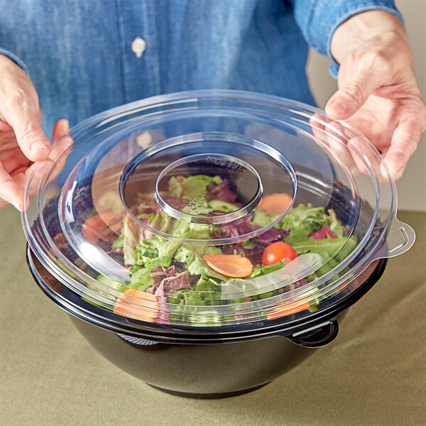 A person placing a clear plastic lid over a Visions salad bowl.
