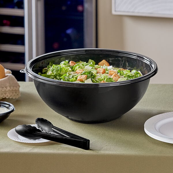 A Visions black plastic bowl filled with salad on a table with a spoon.
