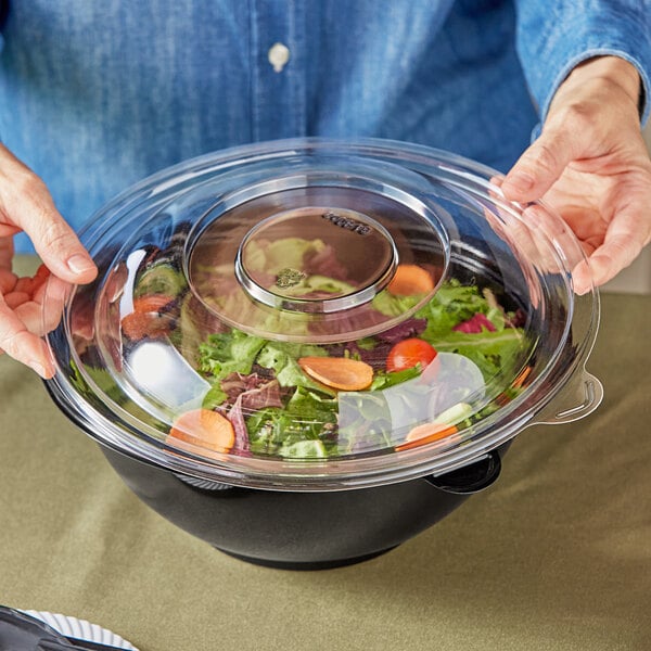 A woman holding a Visions clear plastic dome lid on a bowl of salad.