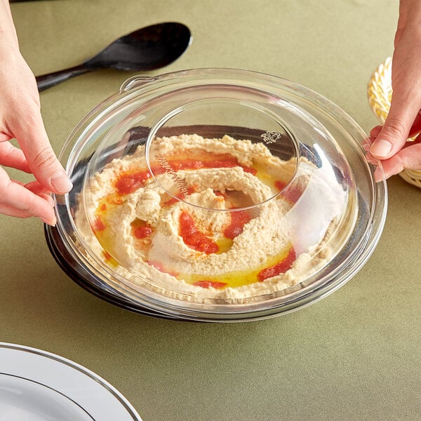 A person holding a bowl of hummus with a clear Visions dome lid.