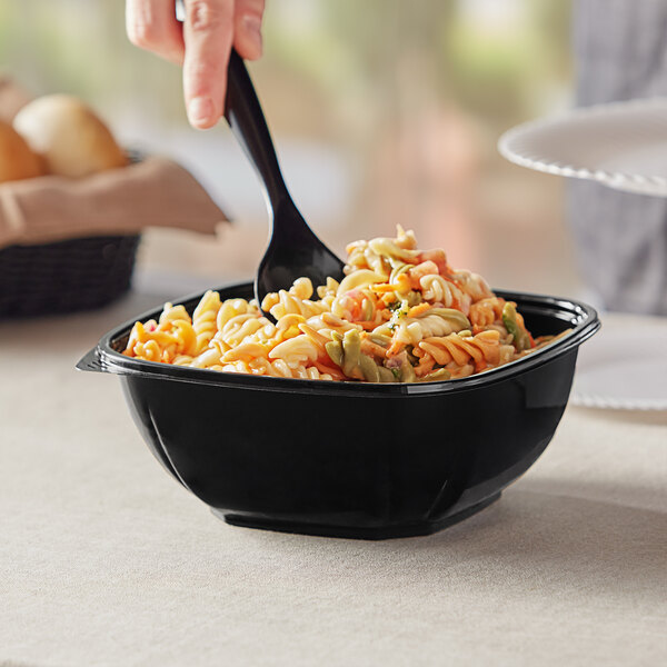 A person serving pasta from a black Visions plastic bowl with a spoon.