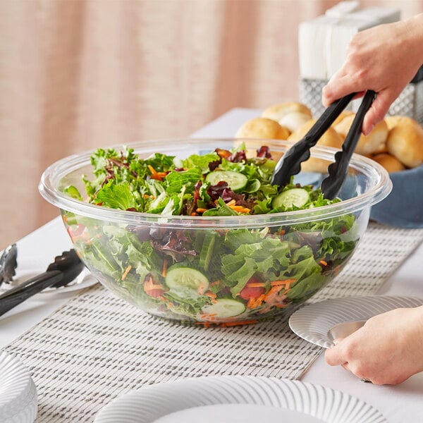 A person using tongs to serve salad from a Visions plastic bowl.