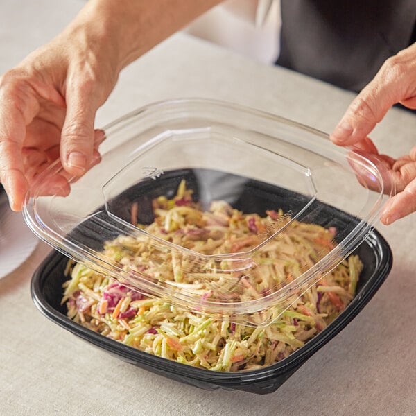 A person holding a Visions clear plastic container of food.