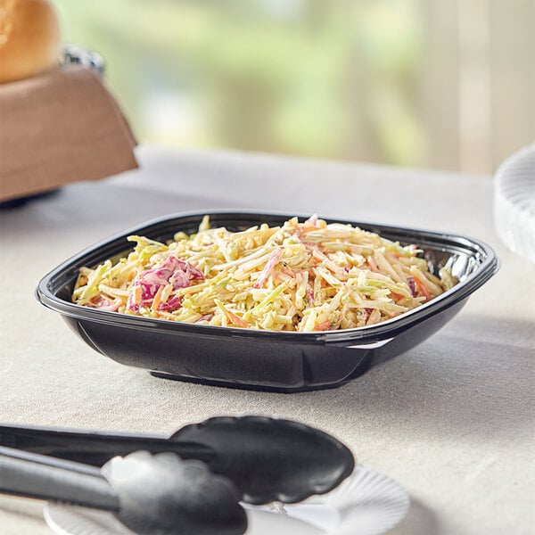 A black Visions plastic square bowl filled with coleslaw on a table.