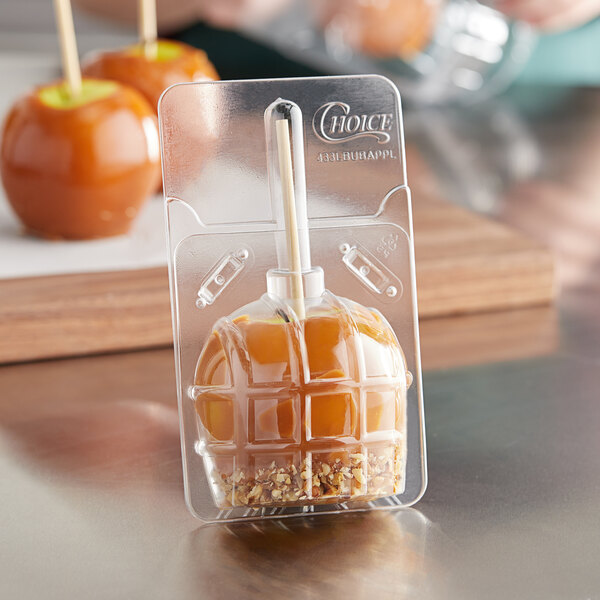 A person holding a caramel apple in a Choice plastic container.