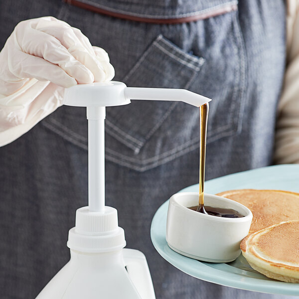 A person using a white Tablecraft condiment pump to pour syrup over a dish of pancakes.