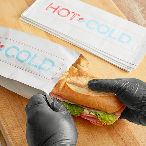 A person in a black glove taking a sandwich out of a Choice insulated bag with hot and cold labels.