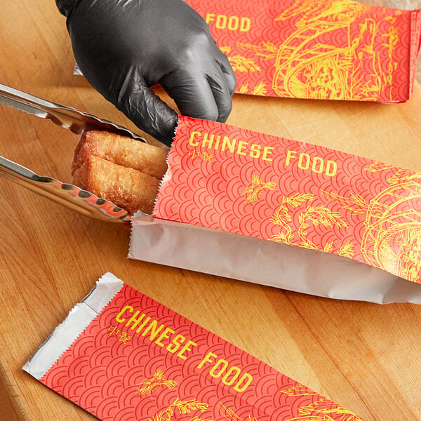 A person in a black glove opening a red Emperor's Select Chinese food bag.