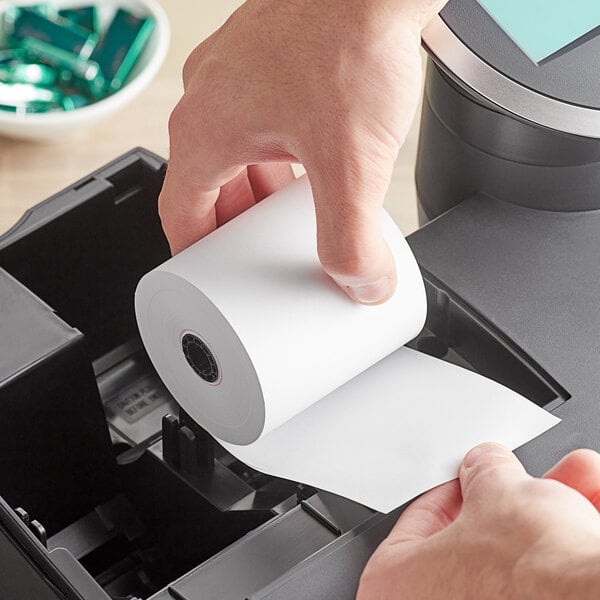 A person putting a white Point Plus Traditional Cash Register paper roll into a printer.