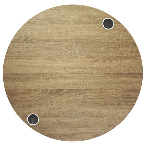 A BFM Seating round wood tabletop with two wireless chargers on it.