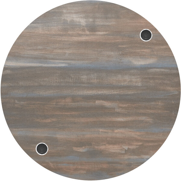 A BFM Seating round chestnut melamine table top with wireless chargers and holes in it.