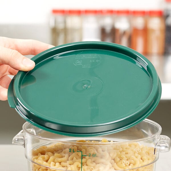 A hand holding a Carlisle green lid over a clear container with pasta inside.