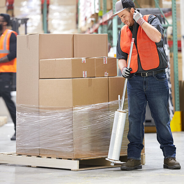 A man in a warehouse using a Lavex Aluminum Nelson wrapper on a pallet of boxes.