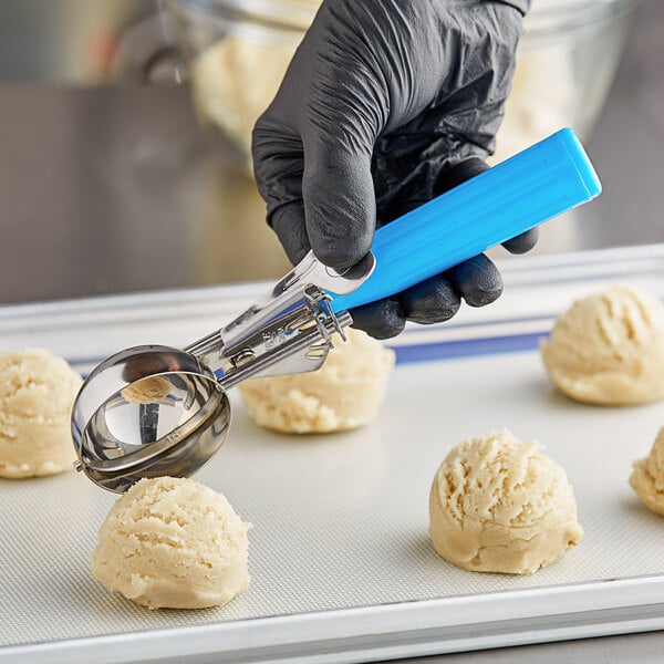A person in black gloves using a blue Choice Thumb Press Disher to scoop a ball of food.