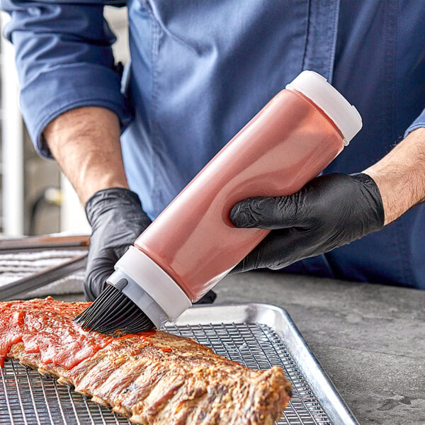 A person with black gloves using a Tablecraft INVERTAtop squeeze bottle with a black brush cap to sauce ribs.